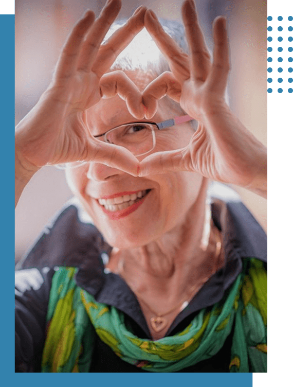 A joyful elderly woman making a heart shape with her hands.